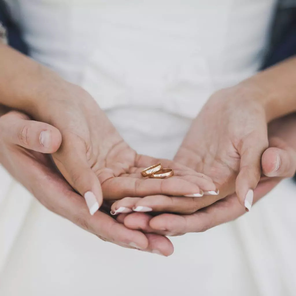 Brudepar holder hender med gifteringer i gult gull i håndflaten 